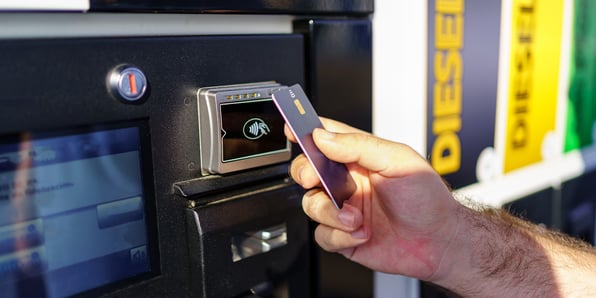 A hand with credit card tapping to pay at gas station pump